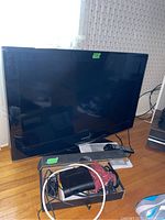 Samsung 32 inch flat screen TV on a small stand with remote control and cables shown.