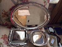 Three silver plated serving pieces including an oval serving tray, rectangular tray, and square serving dish.