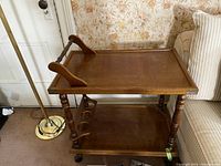 Photo of vintage wooden tea cart showing top and bottom shelves, turned legs, wheels, and side supports
