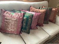 Photo showing six assorted pattern throw pillows arranged on a beige couch, with visible intricate designs and varied colors including pinks, greens, and peach tones.