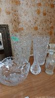 Full view of the crystal items on wooden surface: two vases, one bowl, one bottle with stopper, and another vase with cut designs. Patterns include pinwheel and floral motifs.