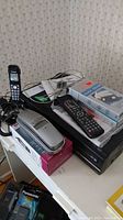 Toshiba VCR with remote, two flip cell phones, VCR head cleaner tape in box, and Panasonic cordless phone on a table.