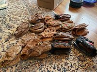 Multiple used leather baseball gloves arranged on a patterned rug showing wear and different brands.