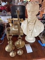 Photo showing bust of Abraham Lincoln, three brass candleholders, and vintage rotary telephone on a wooden table.