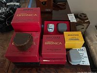 Multiple red Zenza Bronica boxes for two lenses and lens hood alongside yellow Spiratone box and two small gray cases.