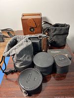 Wooden box pinhole camera at rear with cloth lens pouches and Rolleikin C case in front