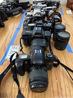 Row of five Canon EOS film SLR cameras on wooden table with two separate lenses on right