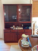 Front view of rosewood hutch showing two glass doors on the upper section, two drawers, and solid-door cabinets below. Hutch contains various items on the surface which are not included.