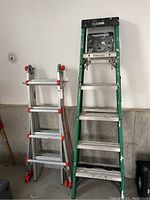 Photo showing two ladders side by side, one aluminum with red accents (Little Giant MegaMax multi-position ladder) and one green metal step ladder (Green Gorilla ladder) with paint splatters.