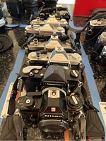 Front view of multiple Nikon and Nikkormat film cameras lined up showing top controls and bodies.