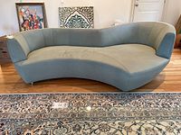 Front view of curved sofa showing shape, sage green pebble-grain upholstery and metal feet