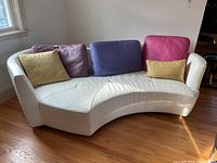 Front view of curved white leather sofa with five accent pillows