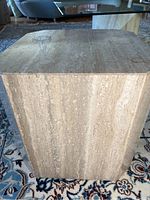 Front and side view of cube-shaped travertine table on patterned rug