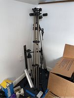 Multiple folded tripods standing next to each other in a corner with cardboard boxes around.