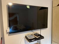 Wall-mounted 55" TV with cables beneath and recorder below on stand