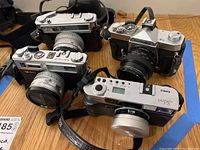 Four film cameras on wooden floor, two Konica and two Yashica.