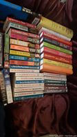 Overhead photo of a pile containing 39 books from two series: Lillian Jackson Braun's "The Cat Who" and J.D. Robb novels. Books are stacked and fanned, showing colorful spines and titles.