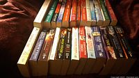 Photo showing a collection of paperback books mostly romance and holiday themed novels, arranged in two rows on a soft surface