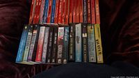 Photo showing the spines of 24 books including thrillers and bright red contemporary Harlequin romance novels.