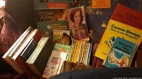 Photo showing assorted books including cartoons like Curious George, Dennis the Menace, Grimm's Fairy Tales, cookbooks and other assorted titles arranged on a couch.