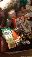 Photo showing assorted wool yarns, craft supplies, metal milk canisters, books, and decorative picks arranged on a dark surface.