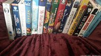 Photo showing 13 miscellaneous VHS movie videos arranged side by side on a red blanket surface.