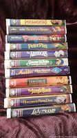 Photo showing a collection of 12 Disney VHS tapes stacked vertically on a purple background.