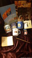 Photo showing collection of royal memorabilia including souvenir books, three commemorative mugs, a soldiers' Bible, and a pencil.