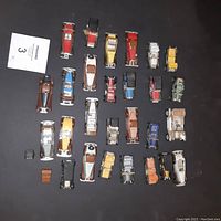 Top view showing 27 toy cars in various colors and styles, arranged on a black surface.