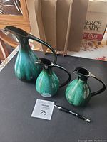 Set of three Blue Mountain Pottery jugs in varying sizes with black handles and green drip glaze on table.