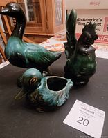 Photo showing three Blue Mountain Pottery pieces on a table: a standing goose figurine, a rooster figurine holding a squirrel, and a duck-shaped planter with a hollow body.