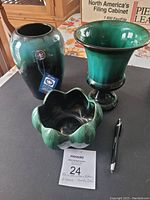 Three Blue Mountain Pottery pieces: two vases and one candy dish placed on a wooden surface with a pen for scale, showing their green to black gradient glaze and varying shapes.