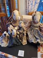 Group photo showing two large bunny fabric door stops and three smaller fabric animal door stops all dressed in vintage style clothing with lace and bells.