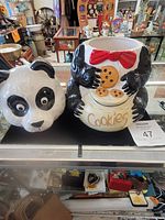 Front and side view of the ceramic panda cookie jar with head lid removed showing the panda holding cookies with a red bow tie detail.