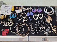 Top-down photo of assorted costume earrings laid out on a black cloth, showing a variety of sizes, shapes, and colors.