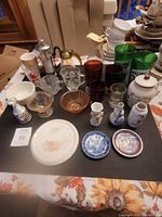 Full view of lot items including various glasses, coffee pot, porcelain vases, bowls, and plates on black surface.