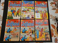 Photo showing six comic books, five Jughead and one Reggie and Me, spread out on a dark cloth on a table with orange floral tablecloth edges visible.