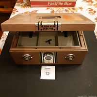 Front view of metal lock box with lid open showing removable tray with compartments and a key inside.