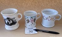 Photo showing all three shaving mugs side by side with a MaxSold catalog card and pen for scale.