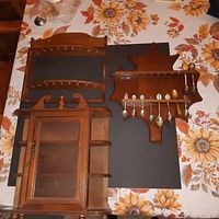 Overview of two wooden spoon holders and one wooden niche shelf with glass door and side shelves placed on a floral tablecloth