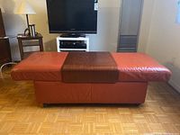 Full view of the orange leather bench featuring a dark wood fitted top section, showing the seating and base with casters.