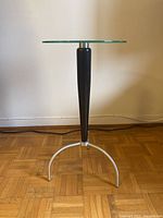 Side view of modern side table showing glass top, black wooden central column, and metal tripod base