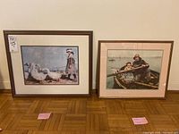 Two framed prints placed on the floor side by side, one larger depicting a girl with geese, the other smaller of man and child in a boat.
