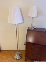 Photo of both lamps side by side showing size difference, brushed metal bases, and white pleated shades.