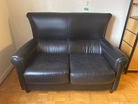 Front view of black leather loveseat with high backrest and rounded armrests. Shows overall shape and condition of sofa.
