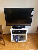 Sony Bravia 32-inch LCD TV model KDL-32XBR9 on top of white TV stand with shelves, showing front view of TV and stand.
