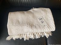 Folded cotton throw blanket on a dark surface showing its waffle weave texture and fringe details.