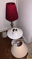 Cluster of three table lamps and two small lamp shades arranged in a corner, showing different styles and materials.