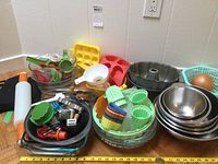 Overall view showing mix of bakeware including metal bowls, silicone molds, plastic storage containers, measuring spoons, cookie cutters, rolling pin