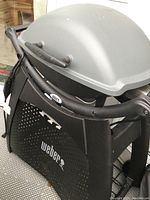 Front view of Weber electric grill on plastic cart stand with closed lid featuring Weber logo